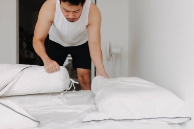 Beyaz kolsuz tişörtlü Asyalı adam katlanır yatağı kanepeye çeviriyor. Yüksek kalite fotoğraf