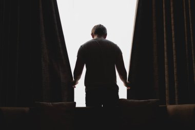 Asyalı adam pencereden manzarayı izlerken perdeyi kapatıyor..