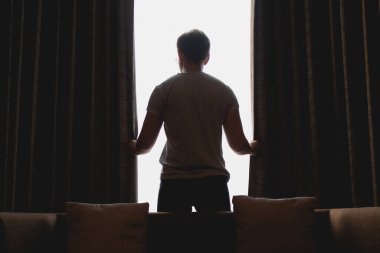 Asyalı adam pencereden manzarayı izlerken perdeyi kapatıyor..