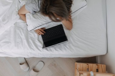 Asian woman sleep on tablet computer on bed in the morning. Early online work. clipart