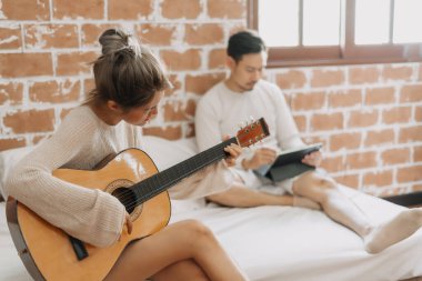 Asyalı kadın, sıcak ve mutlu bir günde erkeğe gitar çalar. Hobi etkinliği kavramı