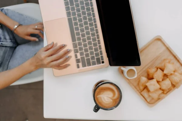 stock image Freelance girl working on laptop with coffee and desserts in the cafe.