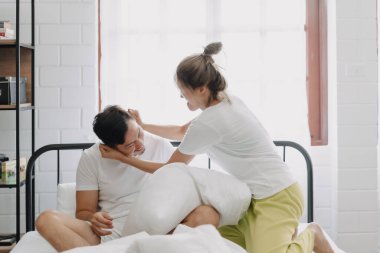 Asyalı karı koca yastık savaşı yapıyor. Komik ve yatakta gülüyorlar..