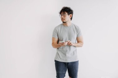 Sıkıcı Asyalı adam cep telefonu uygulaması kullanıyor. Sıkıcı bir şekilde beyazda izole edilmiş..