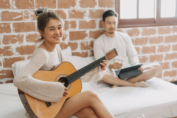 Asiatisk Kvinna Spelar Gitarr Medan Man Frilansar Hemifrån — Stockfoto