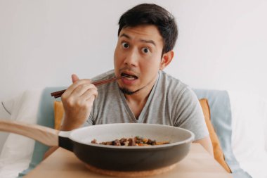 Asyalı adamın yemek çubuklarıyla tavada ev yemeği yediği mutlu yüz ifadesi..