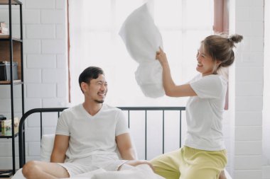 Asyalı karı koca yastık savaşı yapıyor. Komik ve yatakta gülüyorlar..