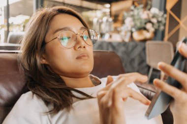 Kafede akıllı telefon kullanan sıkıcı Asyalı kadın..