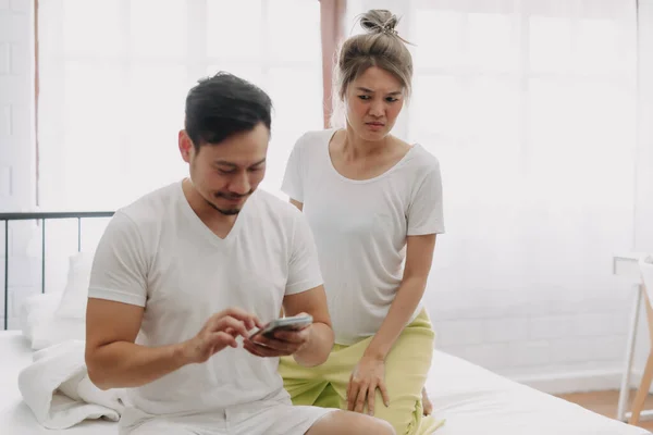 Funny asian couple. Wife peeking husband who chatting on the smartphone.