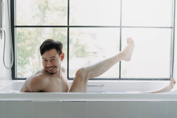 Funny asian man lying in the bathtub showing his leg pretend to be a sexy woman.
