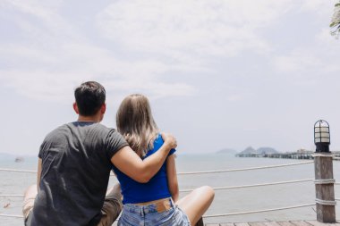 Bir çift Asyalı aşık sarılıp birlikte oturup deniz koyuna bakıyorlar..