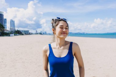 Mutlu gülümse, mavi elbiseli Asyalı kadın güneşli Pattaya sahilinde yürüyor..