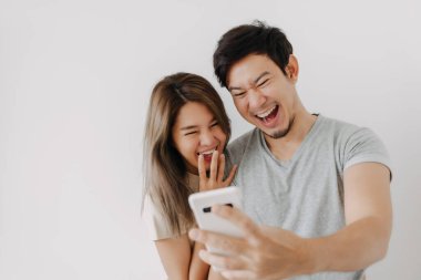 Komik çift Asyalı aşık beyaz telefondan izole edilmiş akıllı telefondaki videoya gülüyor..