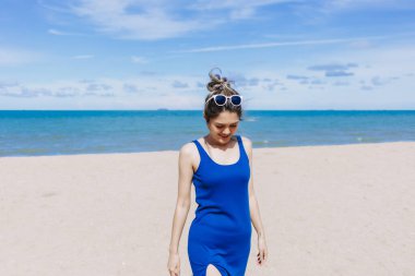 Asyalı bir kadın güneşli sahilde yürüyor. Güneşin teninde yandığını hissediyor..