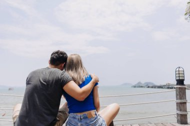 Bir çift Asyalı aşık sarılıp birlikte oturup deniz koyuna bakıyorlar..