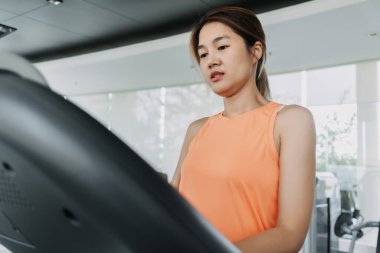 Turuncu spor yapan Asyalı kadın spor salonunda koşu bandında egzersiz yapmak için yürür..