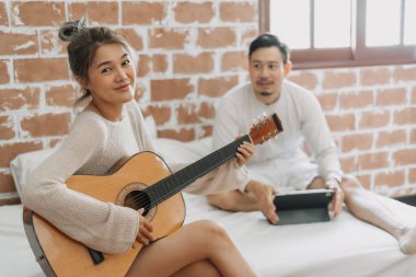 Asyalı bir adam iyi bir hobi haftasonunda kız arkadaşının gitar çalışını dinliyor..