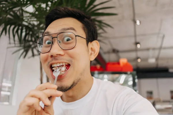 Funny happy face of asian man eating and putting cake into his mouth in the cafe
