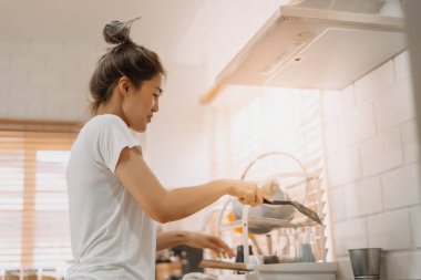 Beyaz tişörtlü Asyalı kadın mutfakta yemek pişiriyor..