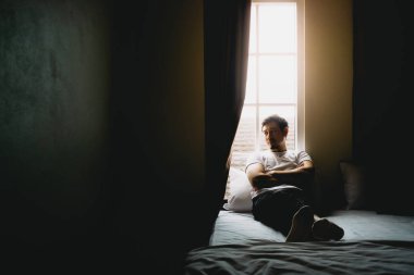 Yalnız bekar bir adam karanlık bir yatak odasında tek başına oturur ve dinlenir..