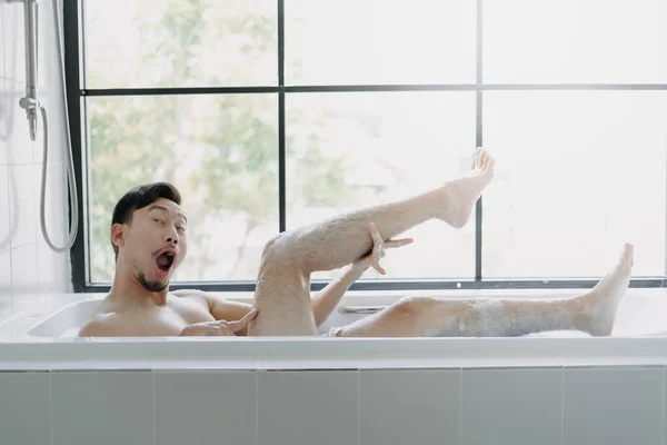 Funny asian man lying in the bathtub showing his leg pretend to be a sexy woman.