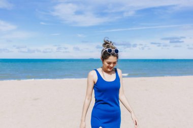 Asyalı bir kadın güneşli sahilde yürüyor. Güneşin teninde yandığını hissediyor..