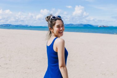 Mutlu gülümse, mavi elbiseli Asyalı kadın güneşli Pattaya sahilinde yürüyor..