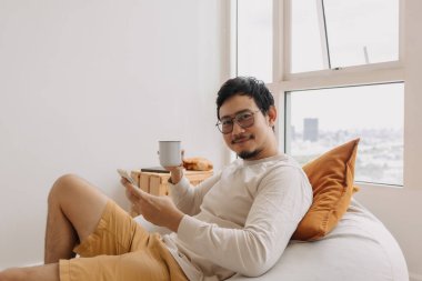 Uzun kollu mutlu Asyalı adam akıllı telefon kullanarak rahat otur..