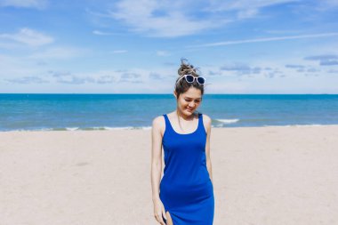 Asyalı bir kadın güneşli sahilde yürüyor. Güneşin teninde yandığını hissediyor..