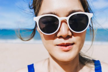 Cilt bakımında parlak güneşli sahilde mutlu Asyalı kadının yüzünü kapatın..