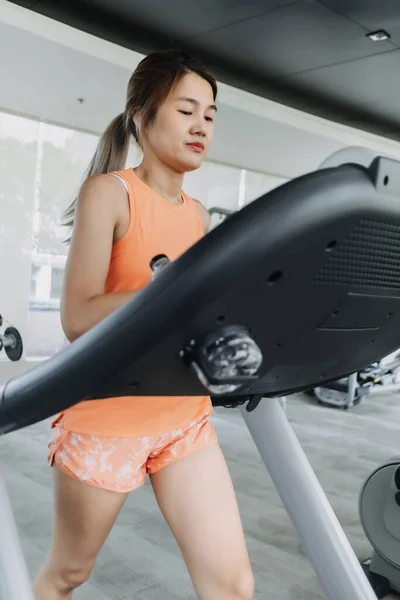 Asian woman in orange sport wears walking for exercise on treadmill in the gym.