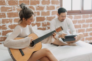 Asyalı kadın gitar çalarken, erkekler evden bağımsız iş yapıyor..