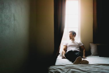 Yalnız bekar bir adam karanlık bir yatak odasında tek başına oturur ve dinlenir..