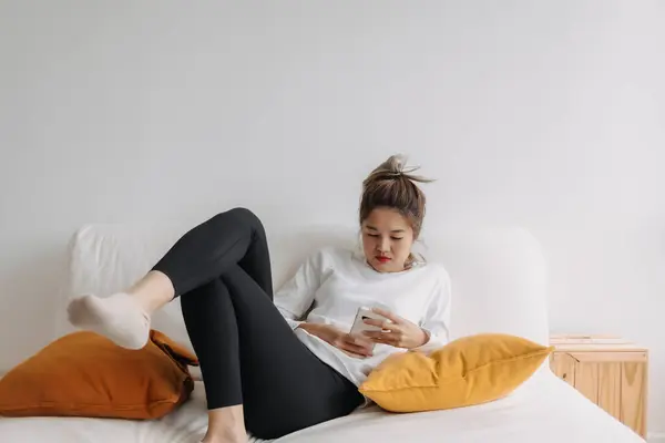 Asian woman using smartphone relaxed on sofa in cold day.