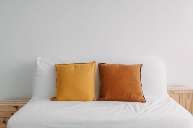 Beyaz oturma odasında kahverengi sarı yastıkla dekore edilmiş basit minimum kanepe..