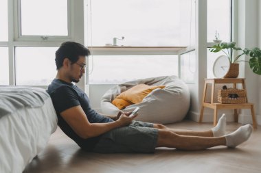 Yalnız Asyalı adam dairesinde tek başına sosyal medya için akıllı telefonu kullanıyor..