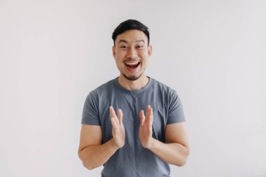 Mavi tişörtlü ve kot pantolonlu mutlu bir Asyalı el çırpıyor.