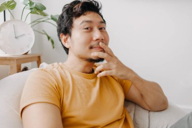 Gülün ve utangaç Asyalı adam sarı tişörtlü fasulye torbasında. Çekici ve rahatlatıcı..