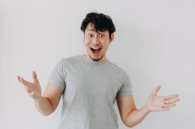 Gri tişörtlü Asyalı adam beyaz arka planda garip, şaşırmış yüz ifadeleri sergiliyor..