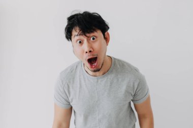 Gri tişörtlü Asyalı adam beyaz arka planda garip, şaşırmış yüz ifadeleri sergiliyor..