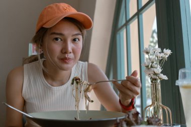 Asyalı kadın kafeteryada turuncu şapka takıp spagetti yiyor..