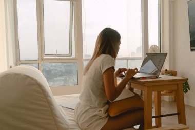 Günlük giysiler içinde, evinde bilgisayarlı bilgisayarıyla çalışan ve daktilo kullanan bir kadın..