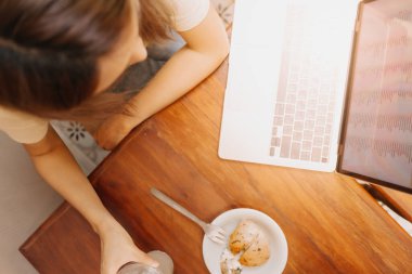Kafede pastayla dizüstü bilgisayarda çalışan Asyalı kadının en iyi görüntüsü..