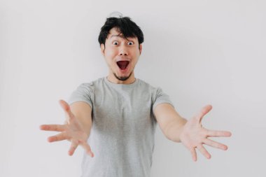 Gri tişörtlü Asyalı adam beyaz arka planda garip, şaşırmış yüz ifadeleri sergiliyor..