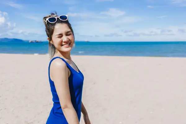 Happy and cheerful asian woman in blue dress on the sunny beach of Thailand.