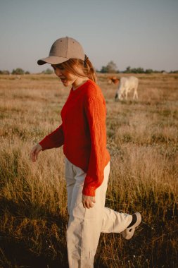 Kırmızı kazaklı mutlu Asyalı kadın otlakta yürüyor sığırları ve gün batımını görmek için.