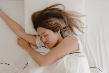 Asyalı kadın beyaz yatakta uyuyor, tamamen uyuyor ve sabaha kadar dinleniyor..