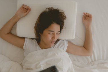 Komik Asyalı kadın cep telefonu elinin yanında uyuyakalıyor..