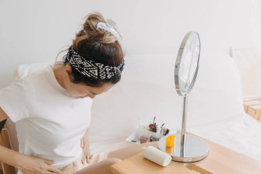 Asyalı Taylandlı kadın aynanın önünde beyaz koltukta otururken güneş kremi kullanıyor ve uyguluyor.. 