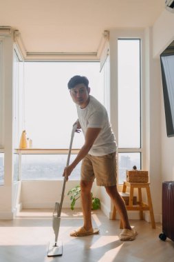 Asyalı Taylandlı adam oturma odasının zeminini temizlemek için paspas kullanıyor ev işleri, ev işi konsepti. evlilik hayatı.